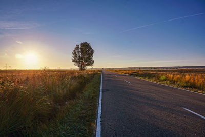 Road amidst field against sky during sunrise