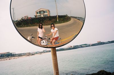 People reflecting on mirror against clear sky