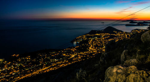 Illuminated cityscape by sea against sky at sunset