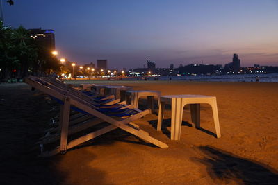 Empty chairs and tables at beach against sky at night