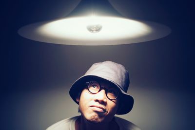 Thoughtful man looking at illuminated pendant light against wall