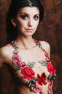 Portrait of shirtless young woman with floral decoration standing against wall