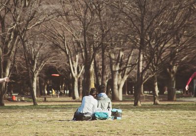 Rear view of couple sitting on field against trees at park