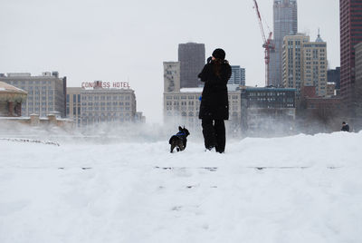Rear view of woman with dog walking on snow in city