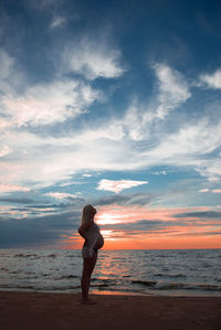 Woman standing on beach against sky during sunset