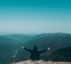 Rear view of man with arms outstretched on mountain against sky