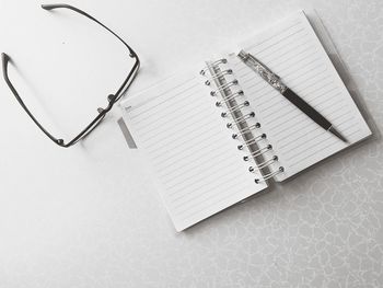 Directly above shot of pen and diary with eyeglasses on white table