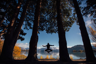 Man jumping amidst trees against lake