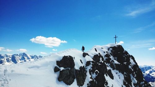 Man by cross on top of snowcapped mountain against blue sky