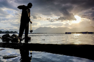 Silhouette of man fishing against sky