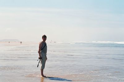 Side view of man standing at beach against sky