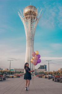 Digital composite image of woman standing with balloons against sky