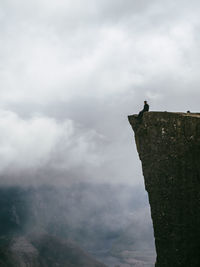 Man sitting on preikestolen cliff against cloudy sky