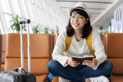 Smiling woman holding passport sitting on chair at airport