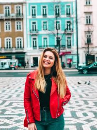 Portrait of smiling young woman standing against building in city