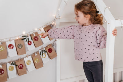 Toddler child gets new advent calendar task, waiting for christmas. festive mood for cute curly girl