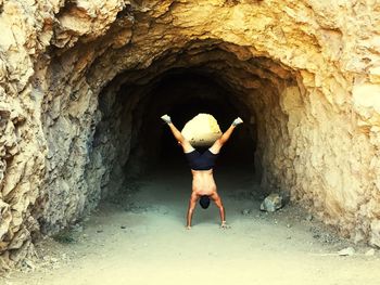 Rear view of man in cave doing a handstand