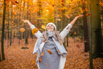 Smiling young woman with arms outstretched in forest during autumn