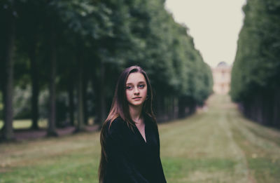 Smiling young woman looking away while standing at park against sky