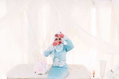 Portrait of young woman siting on seat against textile