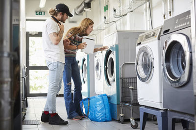 Young man assisting female friend in doing laundry at laundromat