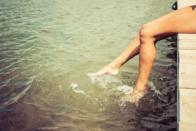 Unrecognizable woman splashing water while relaxing on a pier in summer day. copy space.
