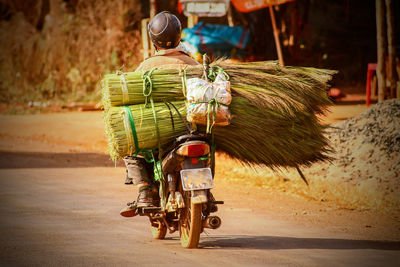 Rear view of man riding motorcycle with brooms on street