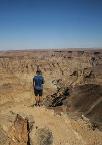 Rear view of man walking on desert against clear sky