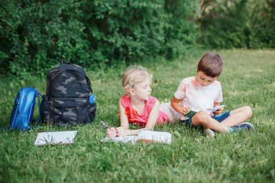 Full length of sibling studying on grass outdoors