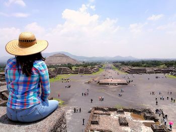 Rear view of woman sitting on rock against sky