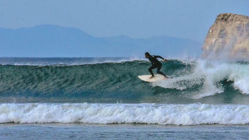 Man surfing in sea against rock formation and sky