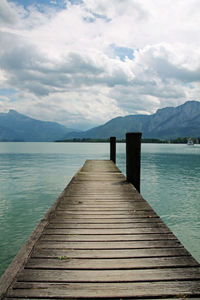 Wooden pier over lake against cloudy sky