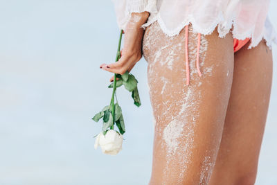 Low section of woman holding rose while standing against sky