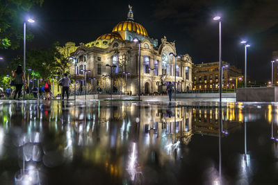 Illuminated palacio de bellas artes reflecting in puddle on street