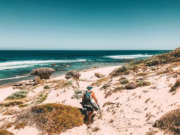 Rear view of man walking at beach against clear sky