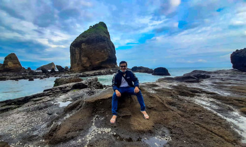 Full length of man on rock at beach against sky