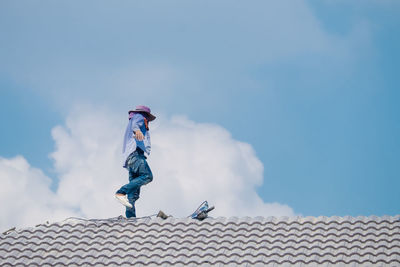 Low angle view of man on roof of building against sky