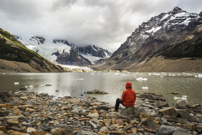 Rear view of woman standing on rock by snowcapped mountain against sky