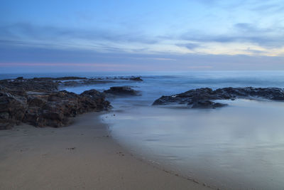 View of calm beach against cloudy sky