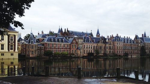 Scenic view of lake by buildings against cloudy sky