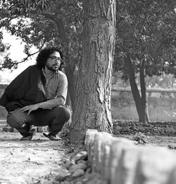 Young man looking away while sitting on tree trunk