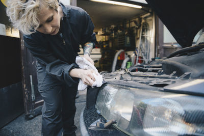 Female mechanic cleaning car headlight outside auto repair shop