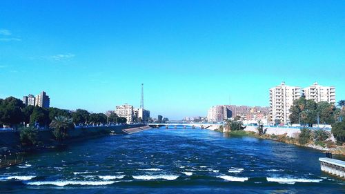 River amidst buildings in city against clear blue sky