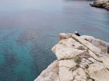 Rear view of man standing on cliff by sea