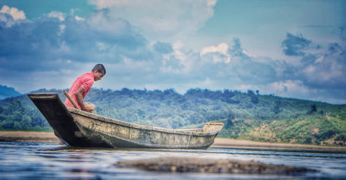 Side view of man sitting in boat on lake against sky