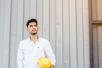 Engineer holding hardhat while standing against corrugated iron