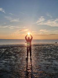 Rear view of man standing on beach against sky during sunset