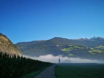 Road leading towards mountains against clear blue sky