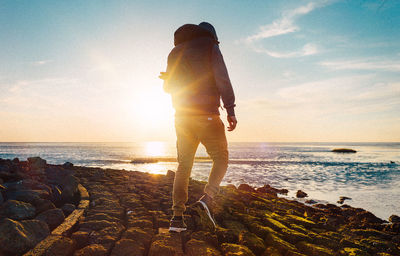 Man walking on beach against sky during sunset