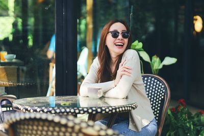 Portrait of young woman wearing sunglasses while sitting on chair